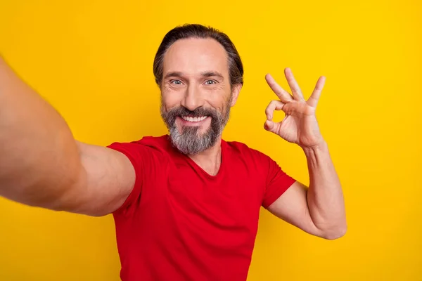 Foto van funky volwassen brunet man do selfie show okey wear rood t-shirt geïsoleerd op gele kleur achtergrond — Stockfoto