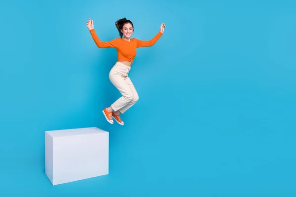 Full size photo of charming good mood female jumping from cube podium isolated on blue color background — Stock Photo, Image