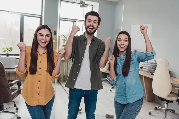 Portrait of three delighted employees raise fists celebrate attainment shout yes office indoors — стоковое фото