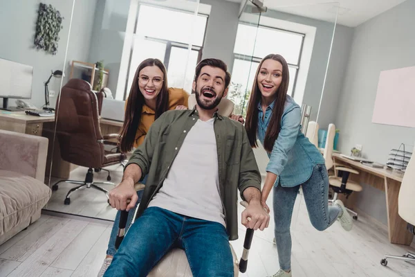 Portrait of satisfied three people fooling around push office chair ride fast speed pause break indoors — Stock Fotó