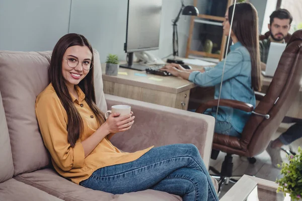 Портрет корпоративных партнёров позитивная дама сидит на диване и наслаждается разработкой кофе-брейка в помещении — стоковое фото