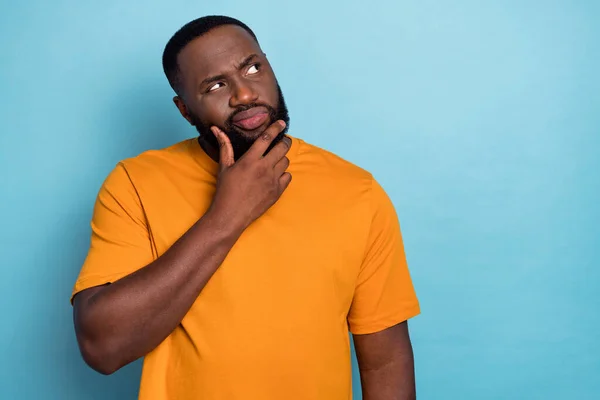 Photo of doubtful unsure guy dressed orange t-shirt looking empty space arm chin isolated blue color background — Stockfoto
