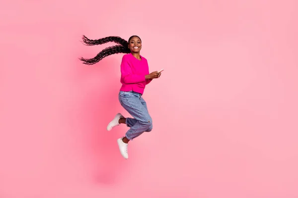 Full size photo of impressed millennial brunette lady hold telephone jump wear pullover jeans shoes isolated on pink background — ストック写真