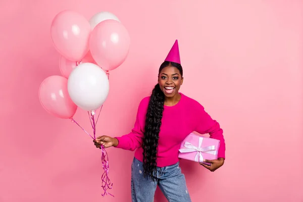 Photo of impressed millennial brunette lady hold balloons present wear cap pullover isolated on pink color background — Zdjęcie stockowe