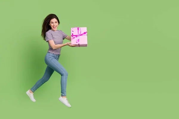 Full length body size view of attractive cheerful thin girl jumping carrying giftbox isolated on bright green color background — Stok fotoğraf