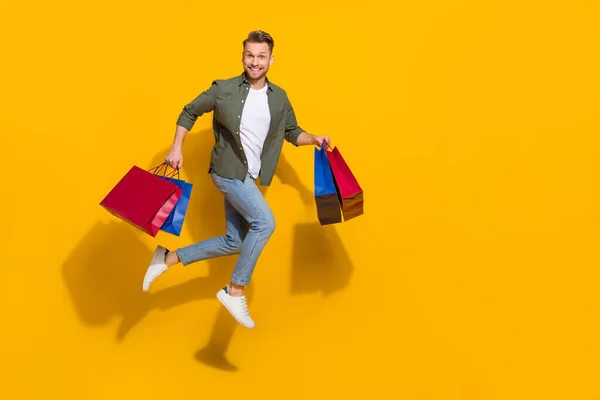 Повнометражний вигляд тіла привабливого веселого хлопця, який стрибає купуючи подарунки речі ізольовані на яскраво-жовтому кольоровому фоні — стокове фото