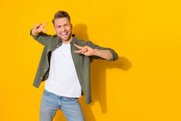 Portrait of attractive cheerful guy dancing having fun showing v-sign isolated over bright yellow color background — Zdjęcie stockowe