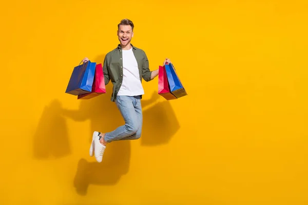 Full length body size view of attractive lucky guy jumping holding things having fun isolated over bright yellow color background — Stockfoto