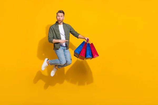Full length body size view of handsome trendy cheery guy jumping showing gifts isolated over bright yellow color background — Stockfoto