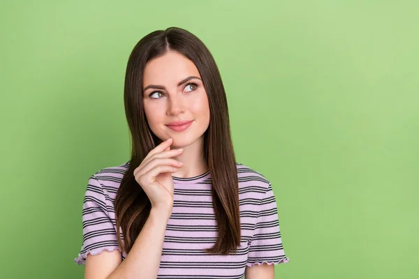 Portrait of attractive pensive cheery brown-haired girl making decision touching chin isolated over bright green color background — Stockfoto