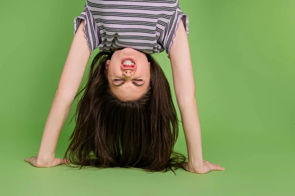 Upside down view portrait of attractive strong girl standing on hands doing exercise isolated over bright green color background — Fotografia de Stock