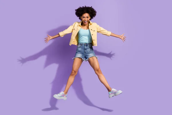 Foto de una mujer muy emocionada vestida con jeans amarillos saltando alto como una estrella aislada color púrpura fondo —  Fotos de Stock