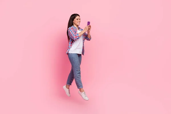 Full body photo of young brunette lady run hold telephone wear shirt jeans sneakers isolated on pink background — Stok fotoğraf