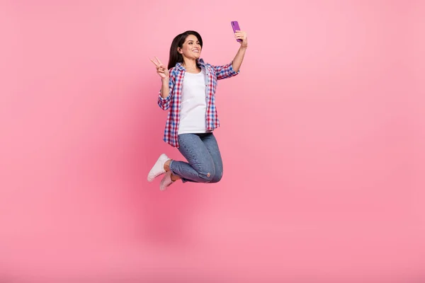 Full size foto van volwassen brunette dame springen doen selfie dragen shirt jeans sneakers geïsoleerd op roze achtergrond — Stockfoto