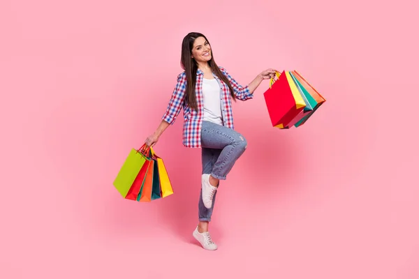 Full length photo of optimistic young brunette lady hold bags wear shirt jeans shoes isolated on pink background — Stock Photo, Image