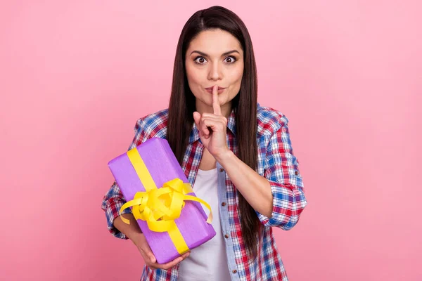 충격을 받은 여자가 체크무늬 셔츠를 입고 손가락 입술로 선물 상자를 분리 된 핑크 색 배경을 들고 있는 사진 — 스톡 사진