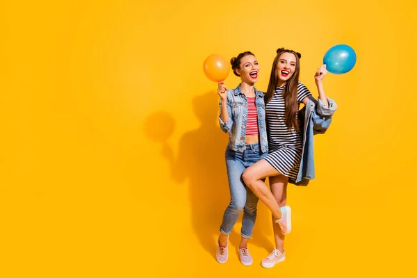 Full body portrait of charming cheerful girls have fun hold air balloons isolated on yellow color background — Zdjęcie stockowe