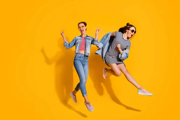 Full size photo of two overjoyed energetic girls jumping demonstrate v-sign isolated on yellow color background — Zdjęcie stockowe