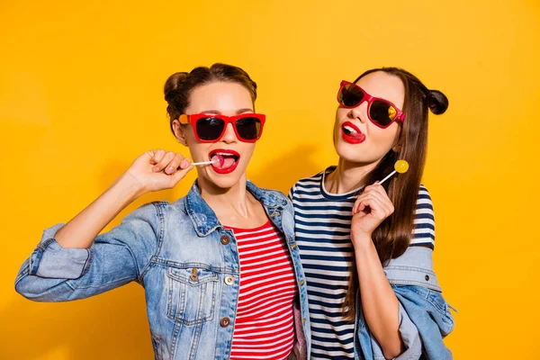 Photo of two funky positive girls lick lollipop candy enjoy free time isolated on yellow color background — Stock Fotó