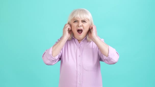 Crazy aged lady hide ears loud music isolated aquamarine color background — Stock Video