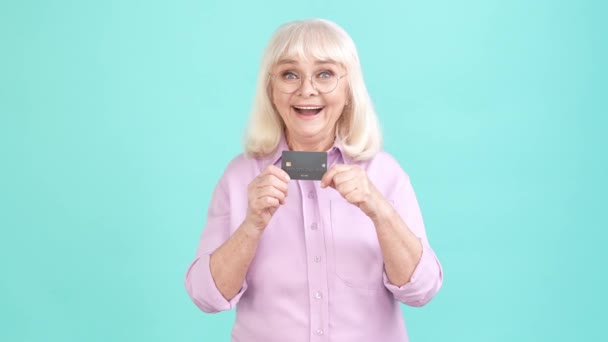 高齢者女性お楽しみ銀行提供預金カード拳アップ隔離されたシアン色の背景 — ストック動画