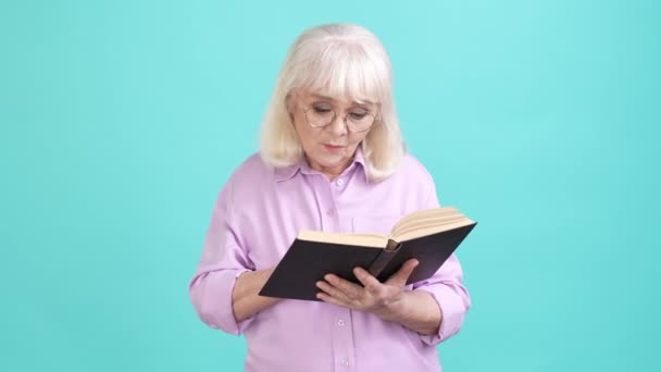 Senhora idosa interessada ler livro didático pensativo isolado cor ciano fundo — Vídeo de Stock