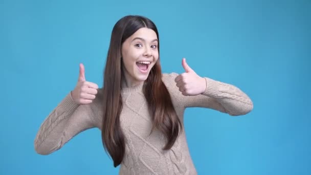 Латиноамериканская девушка-подросток наслаждаться объявлениями сделать большой палец вверх символ изолированный синий цвет фона — стоковое видео
