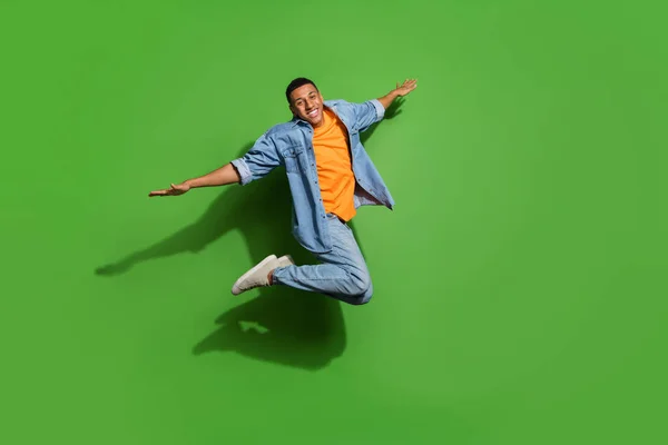 Ganzkörperfoto des gut gelaunten Mannes, der sich frei fühlt und mit ausgebreiteten Armen isoliert auf grünem Hintergrund nach oben springt — Stockfoto