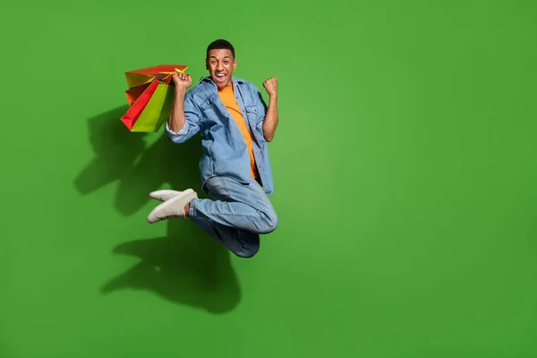 Full length photo of funny man addicted to shopping jumping up in excitement isolated on green color background — Zdjęcie stockowe