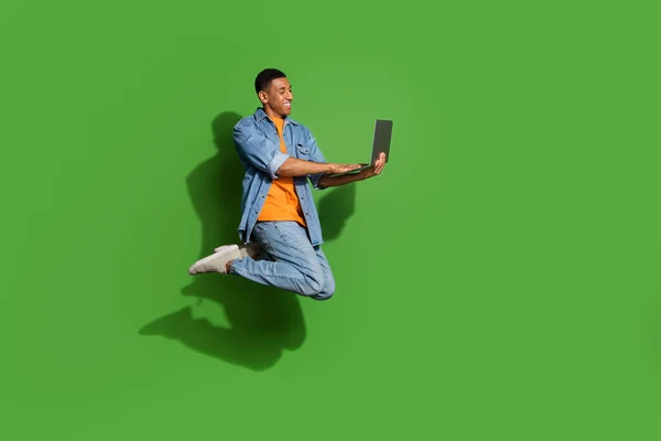 Pełne ciało profil sise zdjęcie wesoły młody inteligentny wykwalifikowany programista skacze z laptopem izolowane na zielonym tle — Zdjęcie stockowe