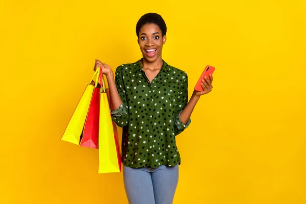 Photo of funky excited androgynous person dressed smart casual chatting gadget holding shoppers isolated yellow color background — 스톡 사진
