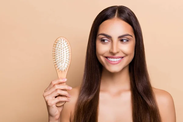 Portrait of attractive cheery girl holding brush strong shine curls daily care solution isolated over beige pastel color background — Stock Photo, Image
