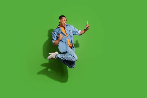 Photo of crazy screaming man jumping up in excitement watch his favorite football team win isolated on green color background — 图库照片