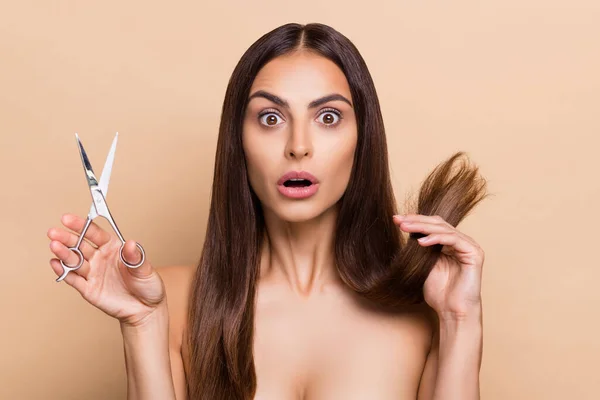 Portrait of attractive worried healthy long-haired girl holding scissors dry ends isolated over beige pastel color background — ストック写真