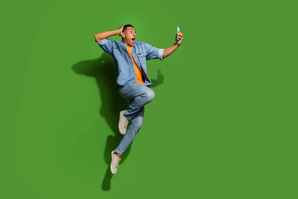 Foto de cuerpo completo del loco impresionado saltando leyendo cosas increíbles en el teléfono aislado sobre fondo de color verde — Foto de Stock