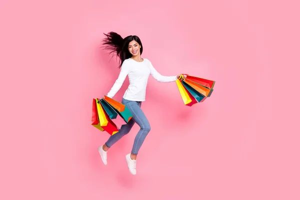 Full body photo of cute millennial lady jump hold bags wear shirt jeans shoes isolated on pink background — Zdjęcie stockowe