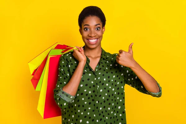 Photo of excited positive androgynous person dressed smart casual showing thumb up holding shoppers isolated yellow color background — ストック写真