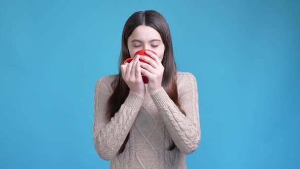 Pozitivní dospívající dáma pít horkou čokoládu izolované modré barvy pozadí — Stock video