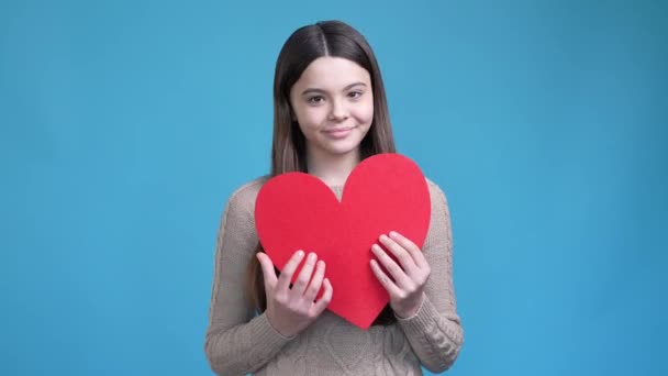 Liebenswert Teen Dame kuscheln große rote Karte Herz isoliert blaue Farbe Hintergrund — Stockvideo