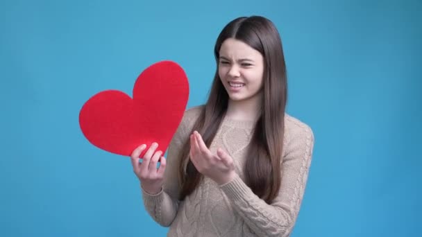 Disappointed teen lady not like red heart card isolated blue color background — Stock Video