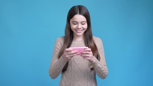 Emocionado juego de chica adolescente gadget puño arriba ganar aislado color azul fondo — Vídeo de stock