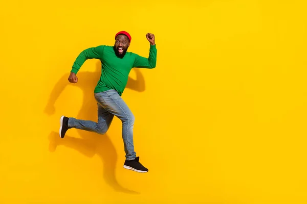 Photo of sportive cheerful crazy guy jump run have fun wear red beanie green shirt isolated yellow color background — Fotografia de Stock
