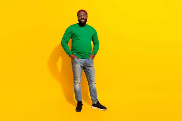 Foto de alegre positivo confiado hombre manos bolsillos desgaste rojo gorro verde camisa aislado amarillo color fondo —  Fotos de Stock