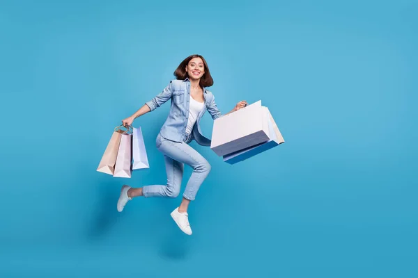 Photo of cute shiny lady dressed denim shirt running fast jumping high holding bags isolated blue color background — Φωτογραφία Αρχείου