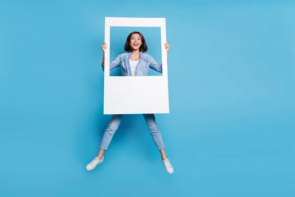 Photo of sweet excited lady dressed denim shirt jumping high holding photo border isolated blue color background — Foto Stock