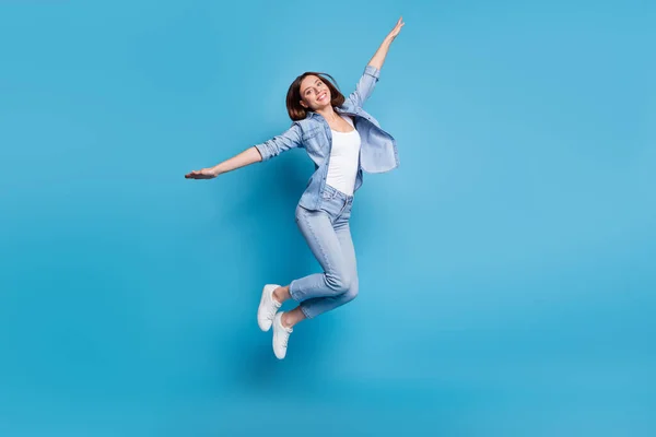 Photo of childish pretty woman wear jeans shirt arms sides jumping high isolated blue color background — Stockfoto