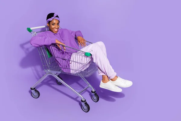 Full length photo of positive bisexual man in trendy hoodie go shopping sit pushcart isolated on violet color background — Photo