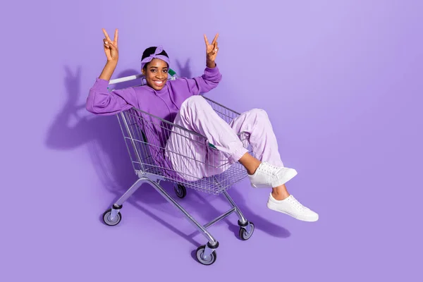 Foto von fröhlich freundlich Transgender Person sitzen Warenkorb zeigen V-Zeichen tragen Stirnband Kapuzenpullover isoliert violette Farbe Hintergrund — Stockfoto