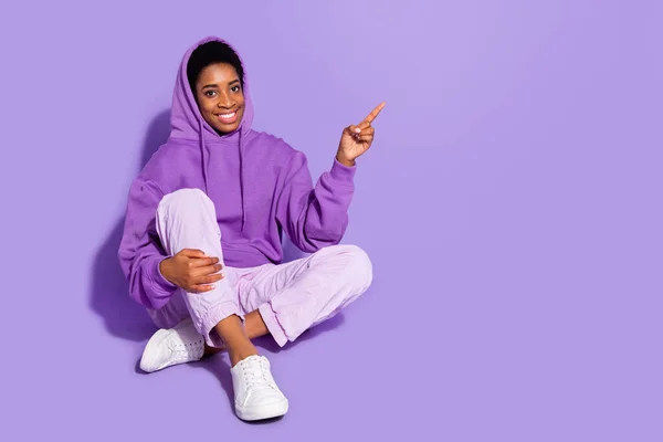 Full length photo of cool millennial lady sit ndex promo wear hoodie παντελόνι παπούτσια απομονωμένα σε μωβ φόντο — Φωτογραφία Αρχείου