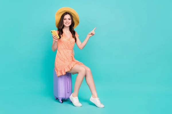 Photo of dreamy pretty lady dressed orange clothes straw hat sitting luggage travel app empty space isolated teal color background — Fotografia de Stock
